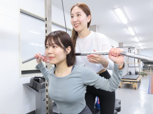 高田馬場・目白・下落合エリアのパーソナルジム『パーソナルランド』で、女性トレーナーがスクワットの正しいフォームを丁寧に指導している様子。初心者も安心して筋力トレーニングに取り組めるパーソナルサポート。